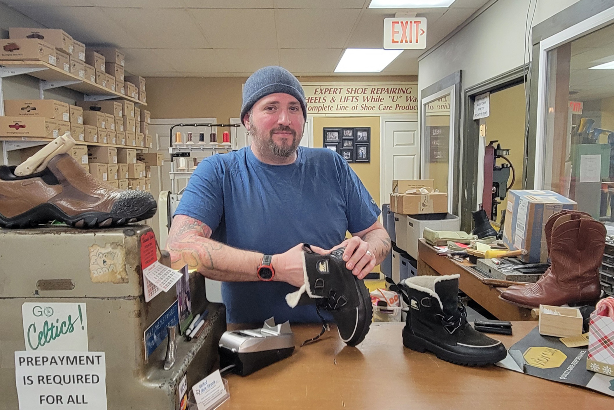 مردی که حبوبات به تن دارد یک جفت کفش را در یک مغازه تعمیر کفش نگه می دارد