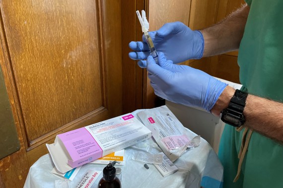 A doctor wearing teal scrubs and purple latex gloves prepares an injection of buprenorphine.