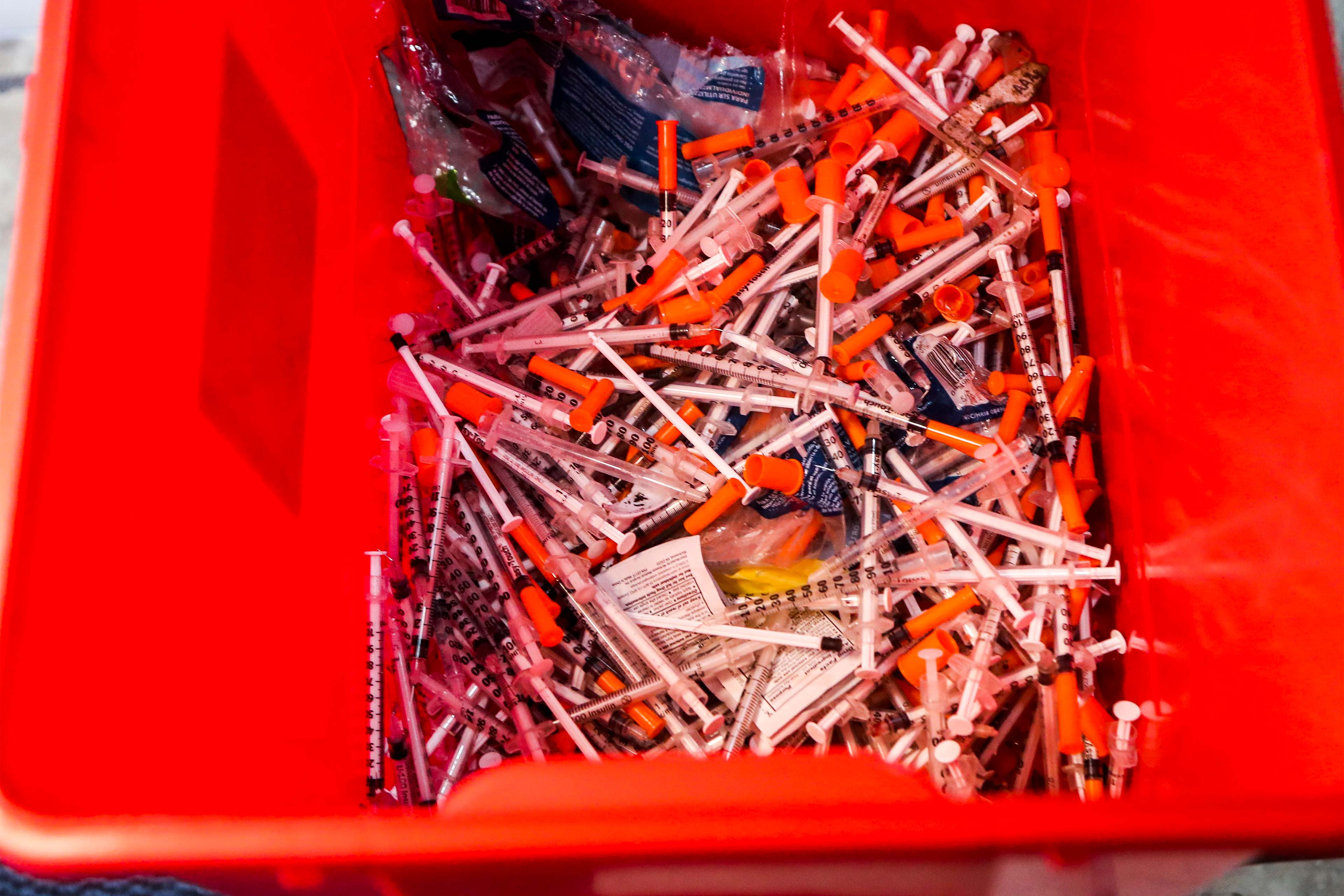A photo of a red biohazard container filled with used needles.