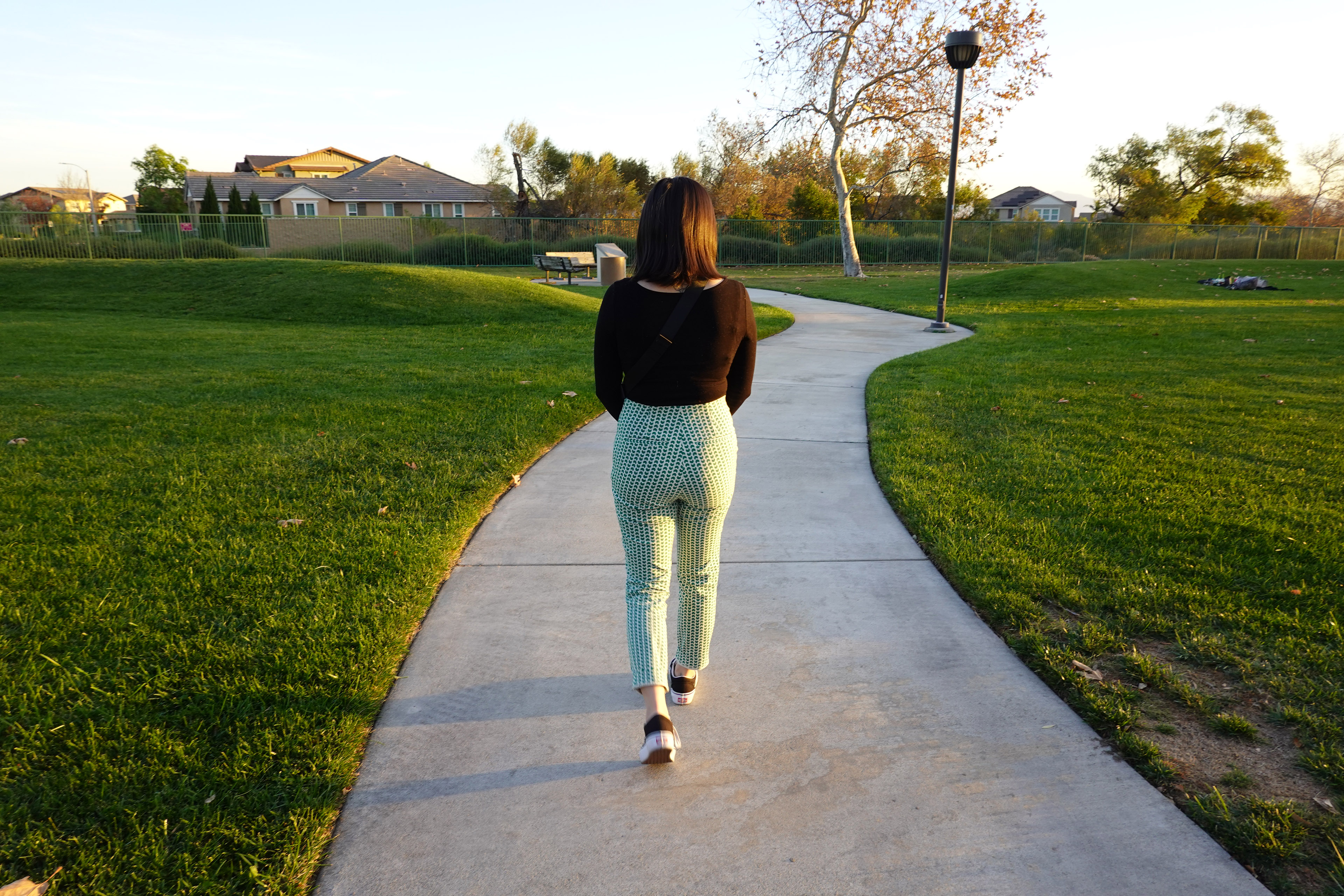 Deanna Gomez walks away from the camera on a paved walkway between two grassy areas.