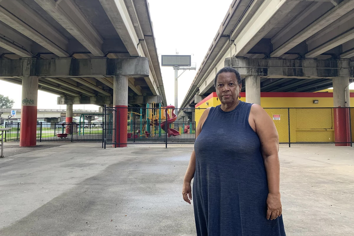 Amy Stelly stands beneath the Claiborne Expressway on July 18, 2023. A playground is visible between the two highways in the distance behind her.