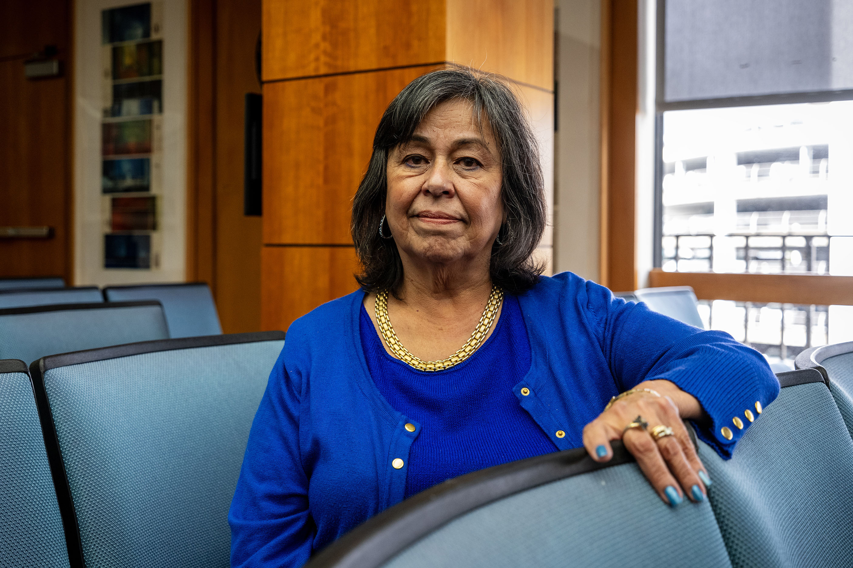 A portrait of Jane Garcia. She sits between rows of blue padded chairs in a professional setting.