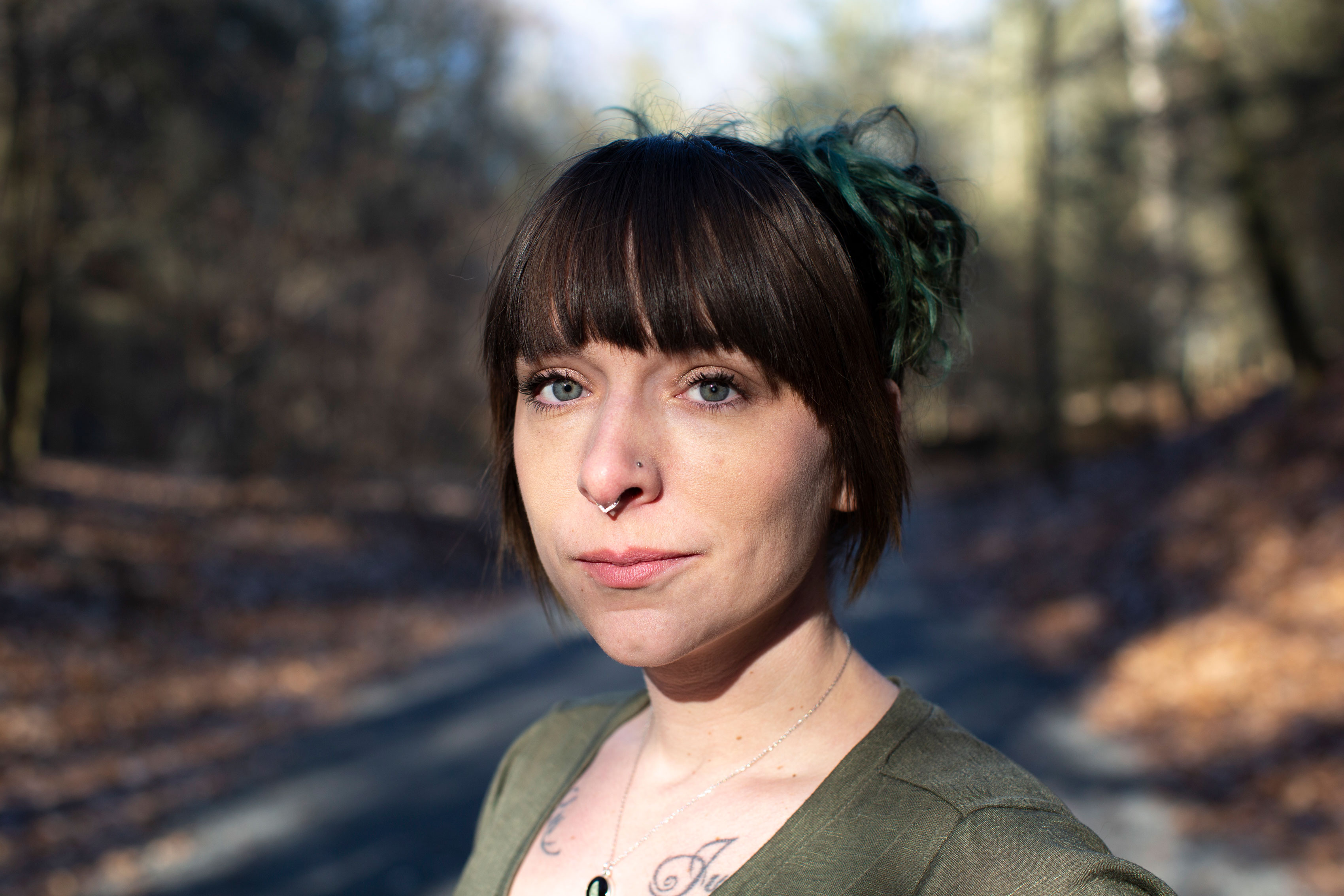 A close-up image of a woman standing outside in the woods and looking at the camera.