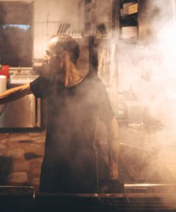 A photo of a man working in a steamy restaurant kitchen.