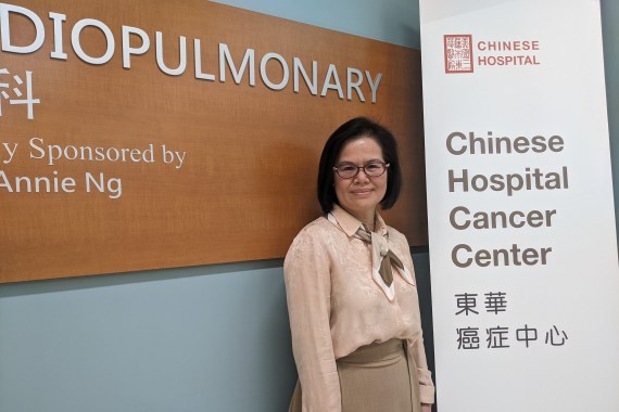 Jian Zhang stands beside a large, vertical sign that says, "Chinese Hospital Cancer Center"