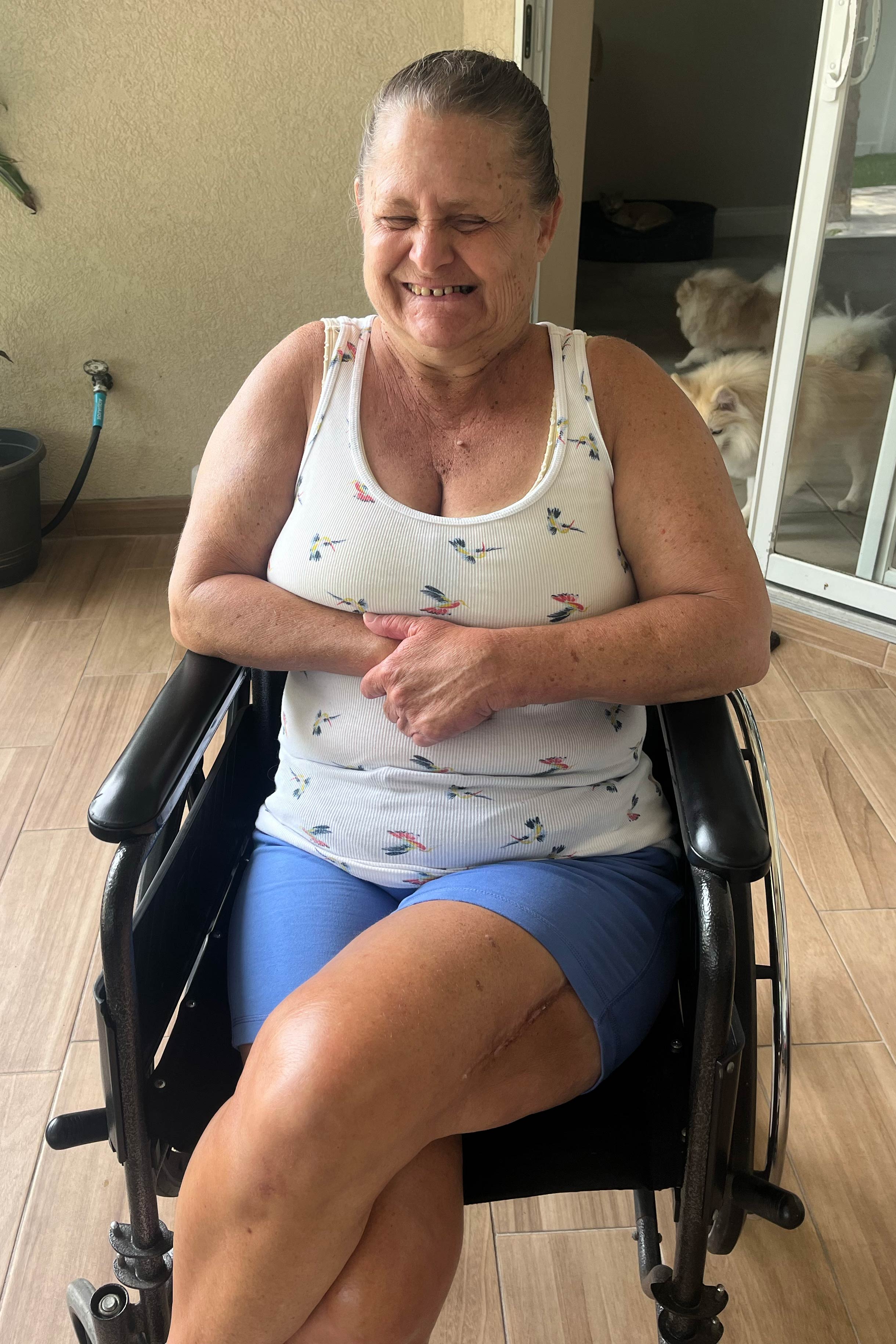 A photo of a woman smiling and sitting in a wheelchair indoors.