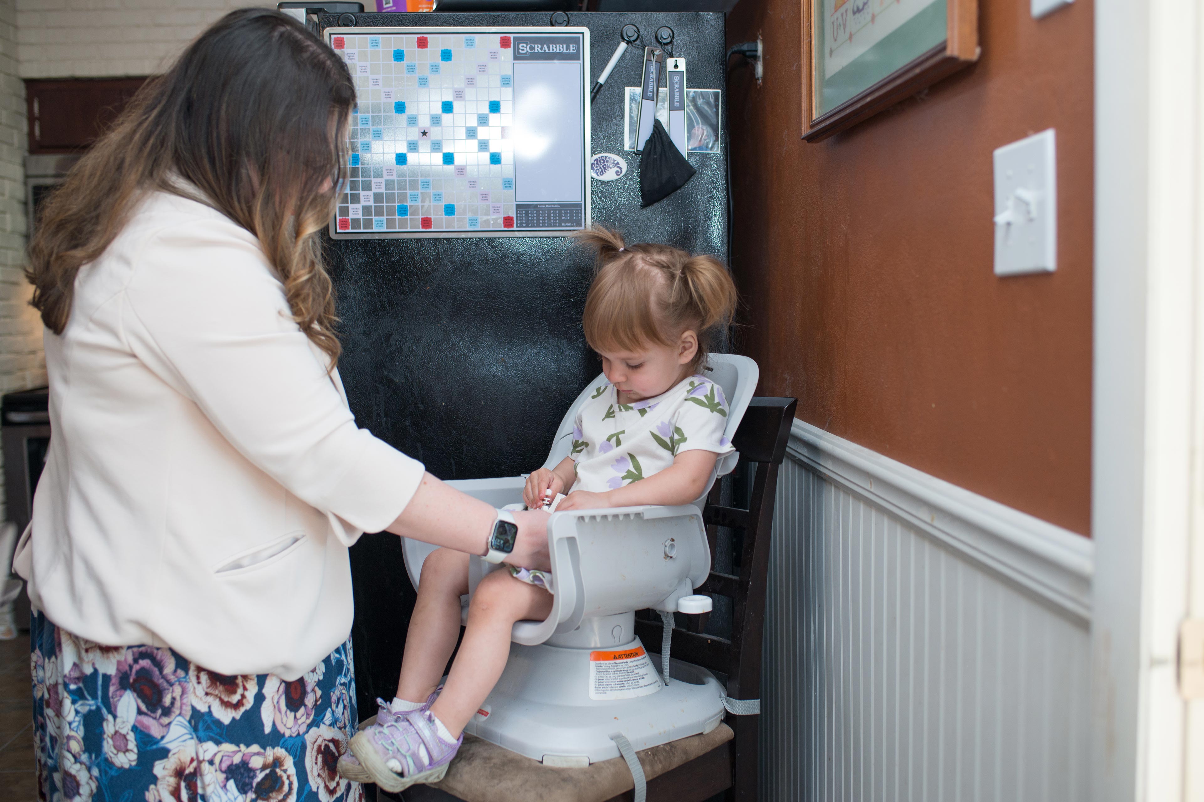 A photo of a mother strapping her young daughter in a high chair.