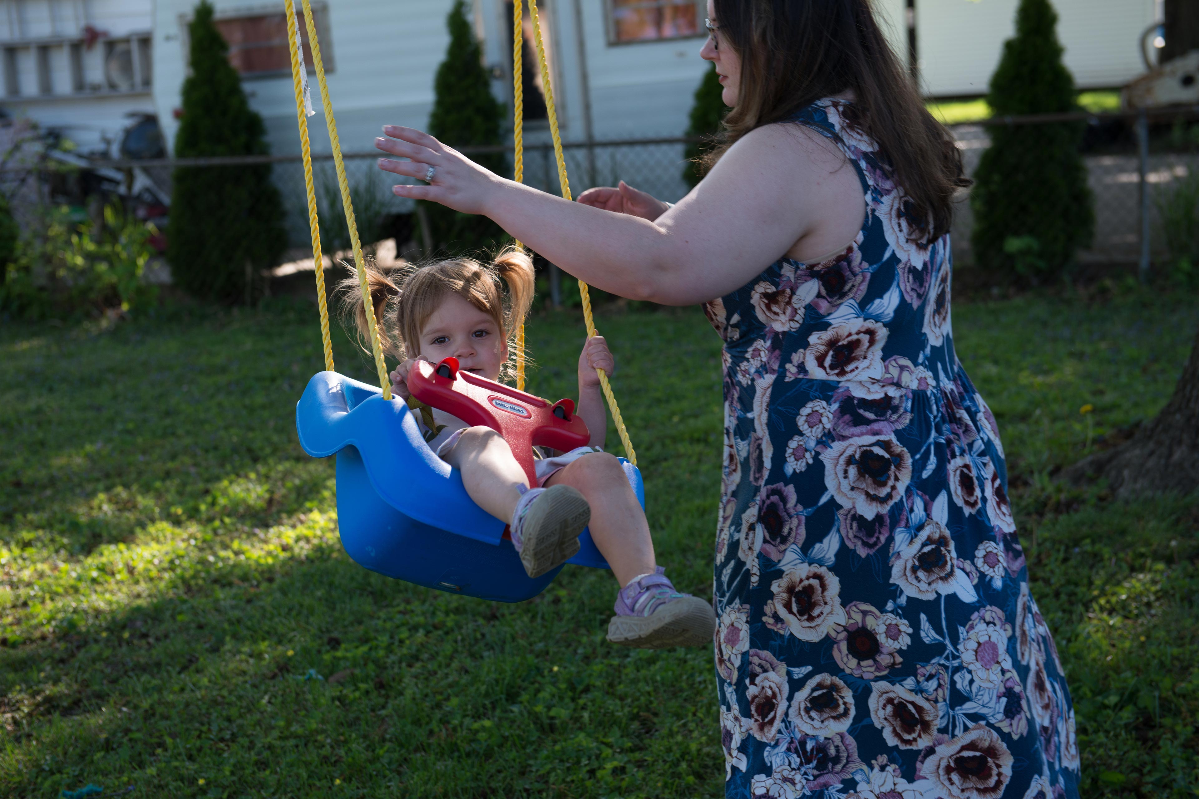 A photo of a mother pushing her toddler daughter on a swing.