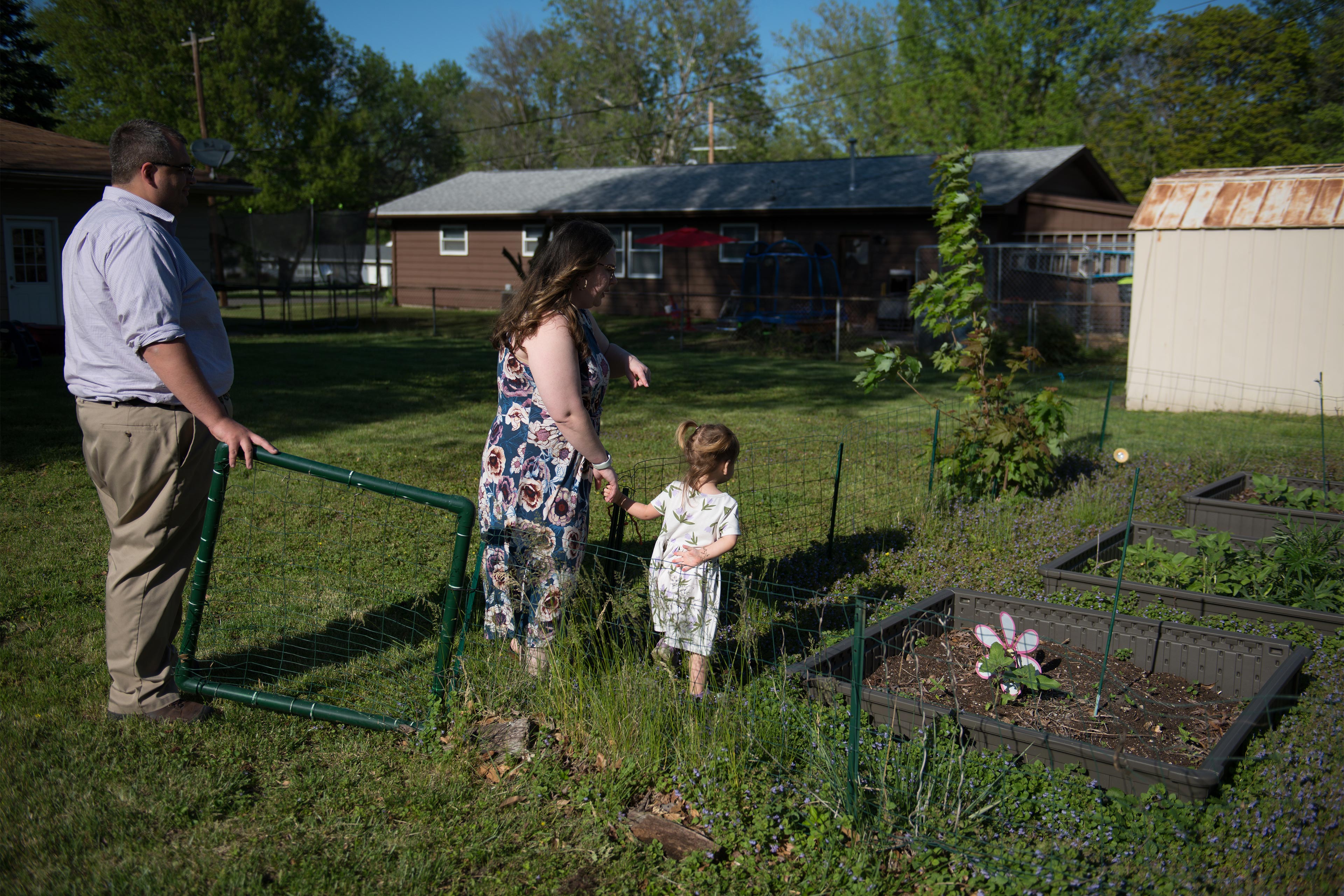 A photo of two parents showing their toddler daughter a garden in their yard.