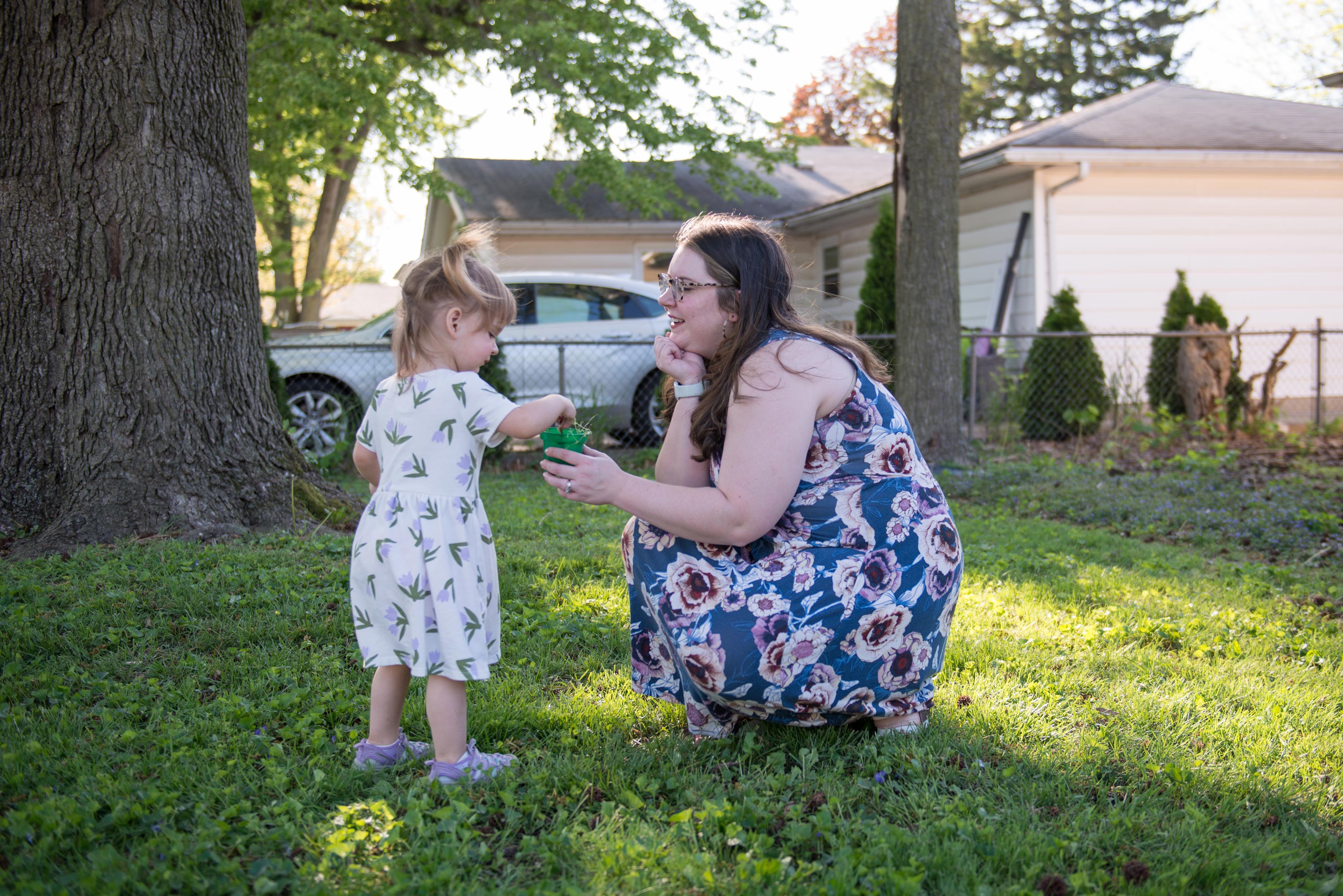 A photo of a mother showing a small planter to her daughter outside.