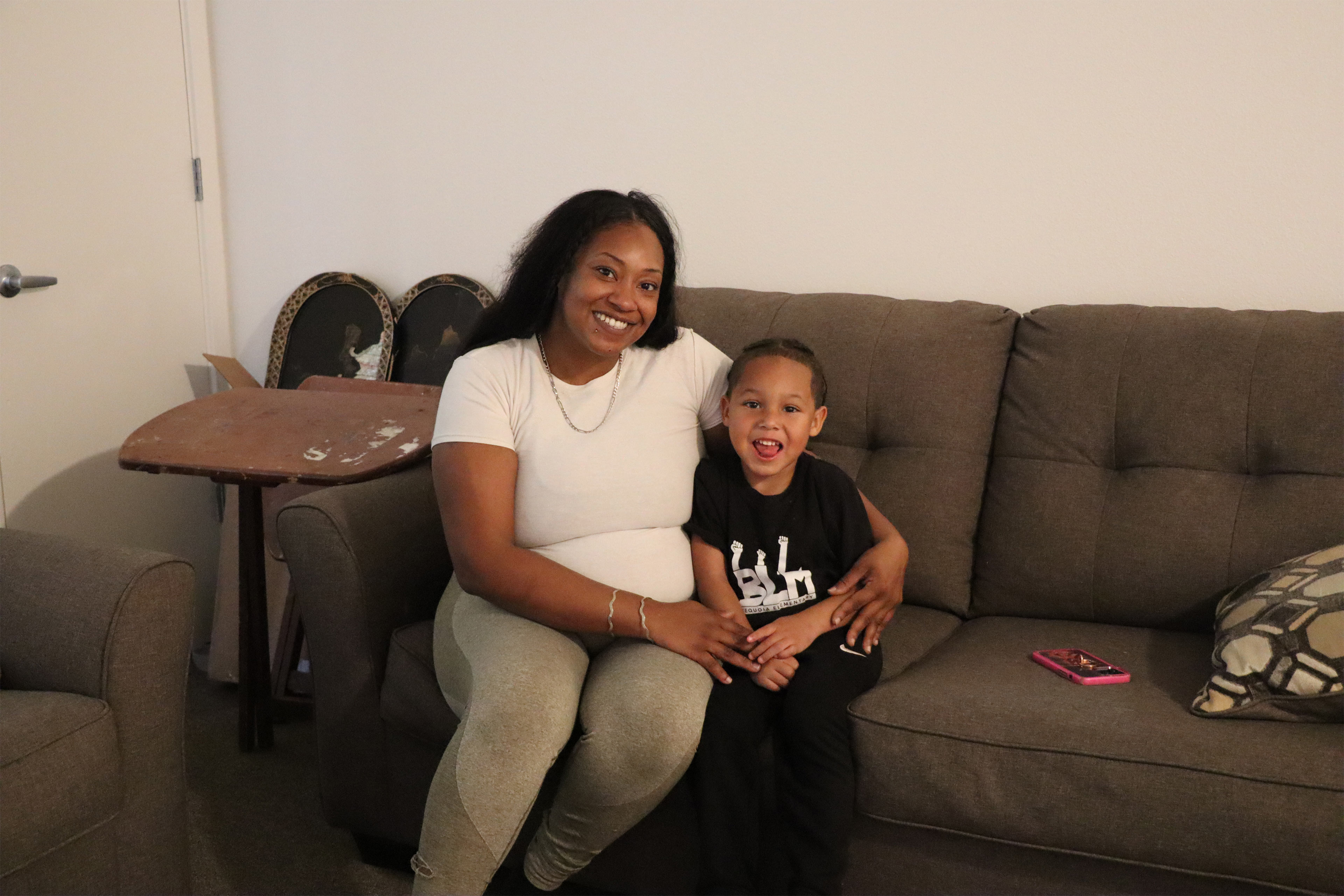 A woman and her young son sit on a couch and smile at the camera.