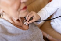 A senior woman has her heartbeat checked by a medical professional with a stethoscope.
