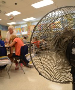 A photo of a fan setup in a classroom as a teacher helps students with their work.