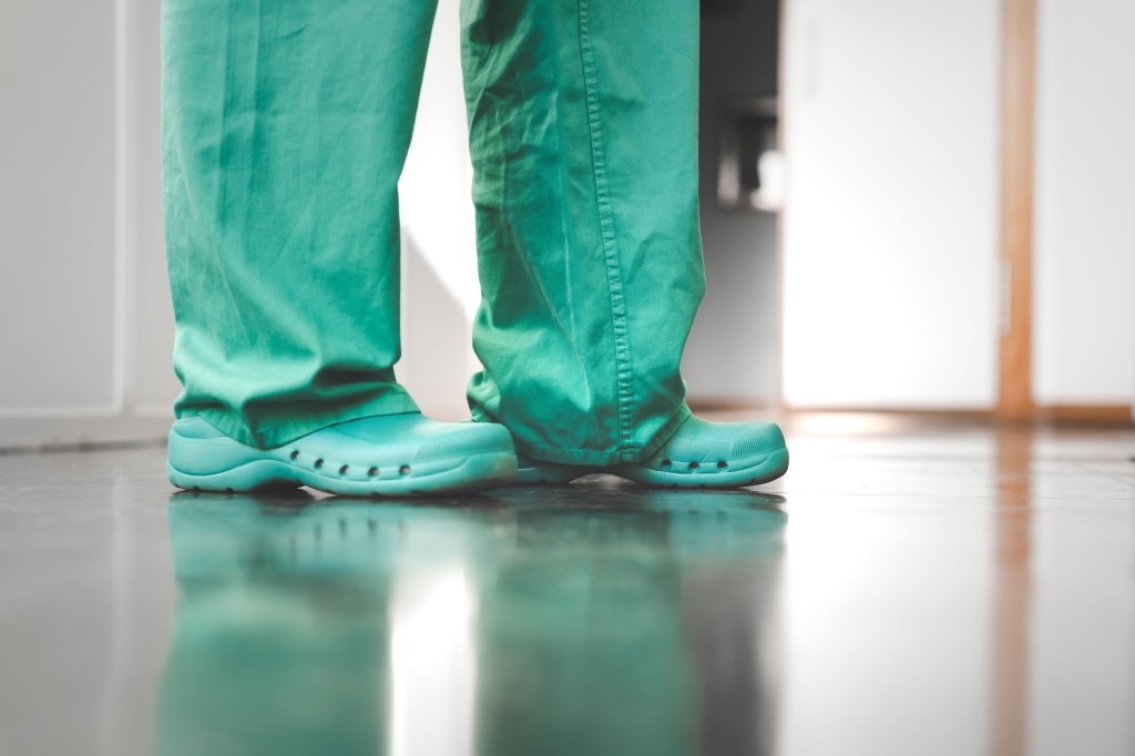 A person wearing green scrubs is photographed from the knees down.
