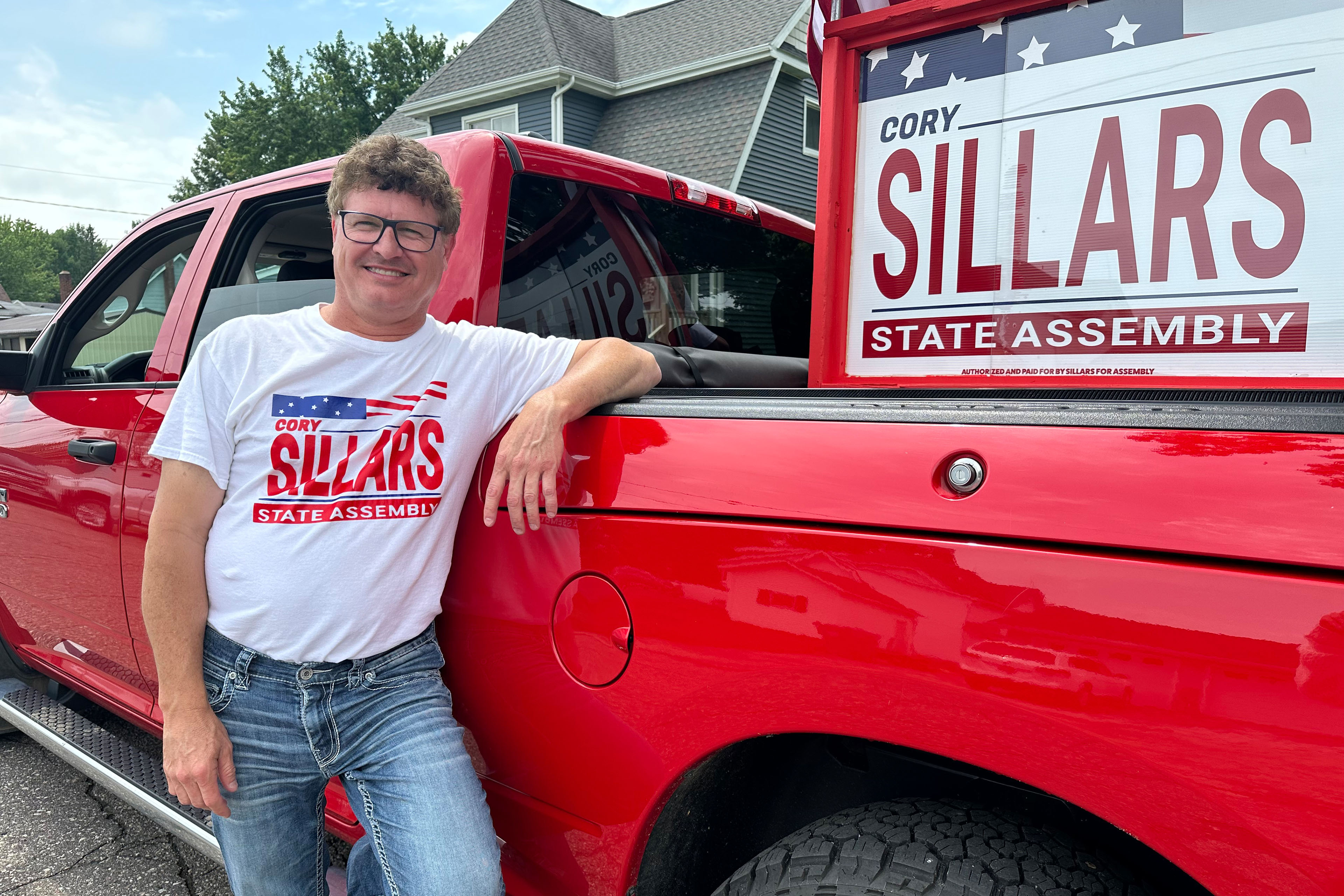 Cory Sillars, a Republican candidate for the Wisconsin State Assembly, stands beside a bright red truck. There is a campaign sign with his last name attached to the back of the truck.