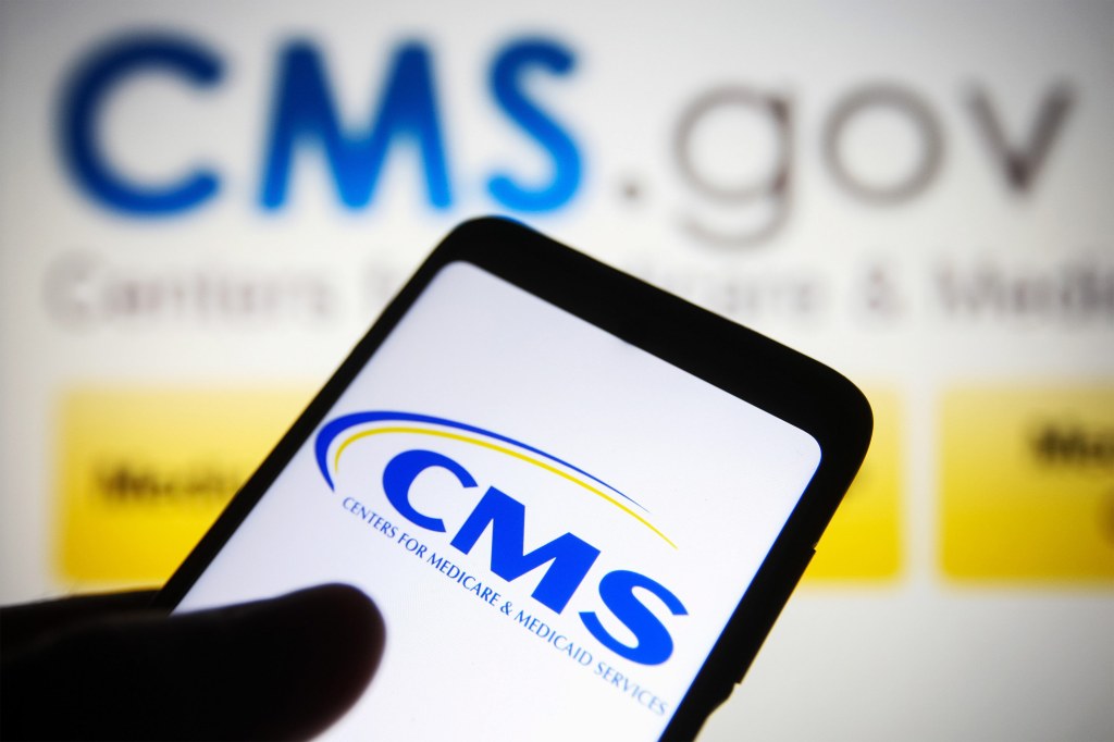 A photo of CMS's logo pulled up on a phone and on a monitor behind up.