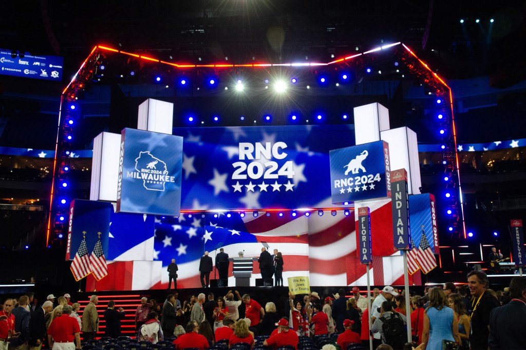 A photo of brightly-lit stage with screens reading "RNC 2024." A crowd is gathered in front of the stage.