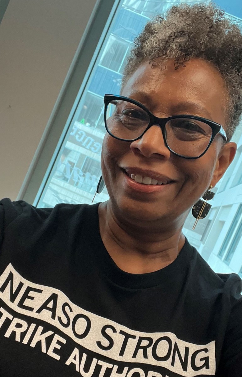 A woman wearing glasses and a t-shirt that reads "NEA SO STRONG"