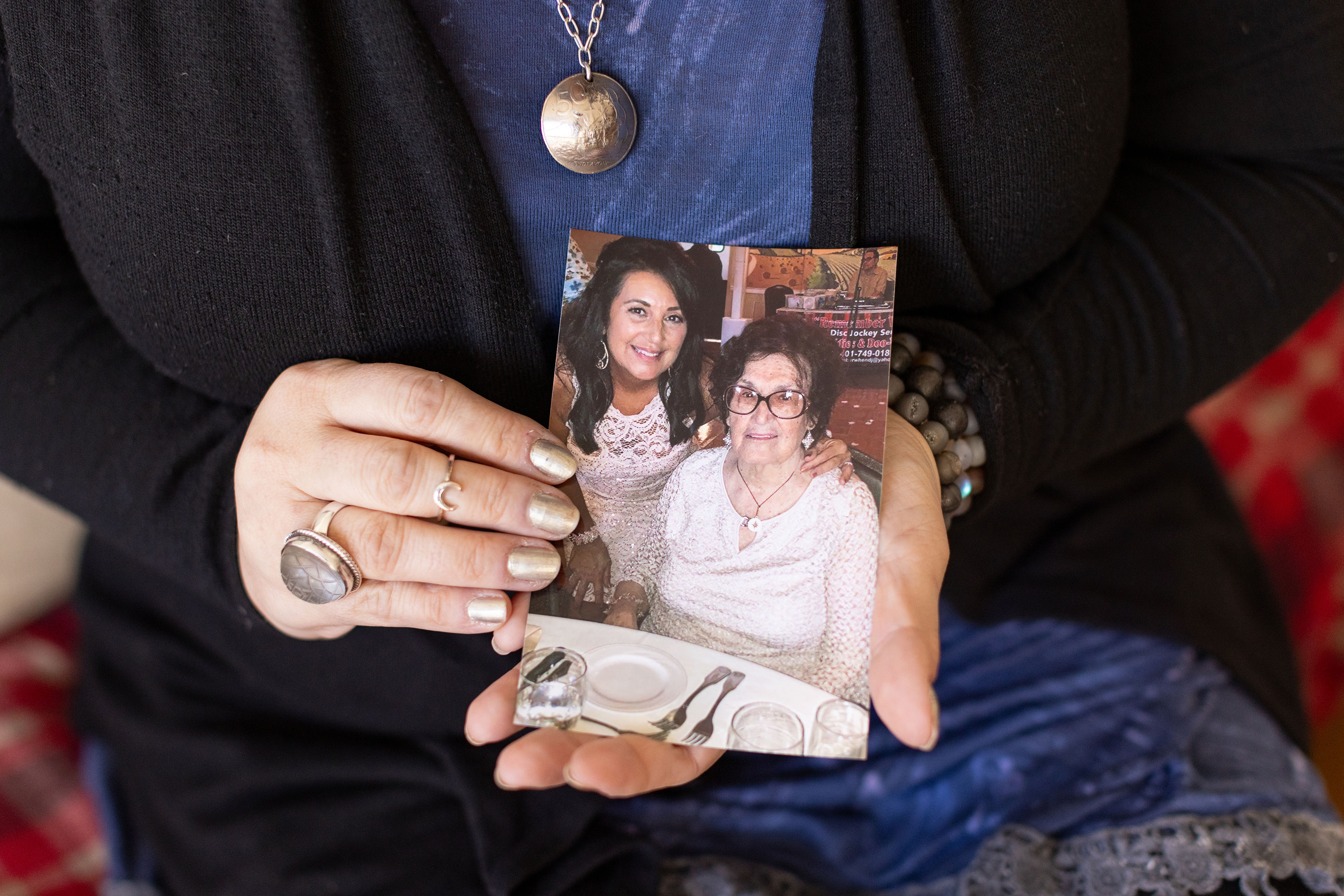 A woman with gold-painted nails holds a photo of a young woman and older woman together at a restaurant