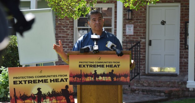 A man, Xavier Becerra, stands behind a podium behind a sign that reads "Protecting Communities from Extreme Heat"