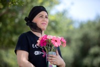 A portrait of a woman wearing a black scarf around her head, holding a vase of pink flowers.