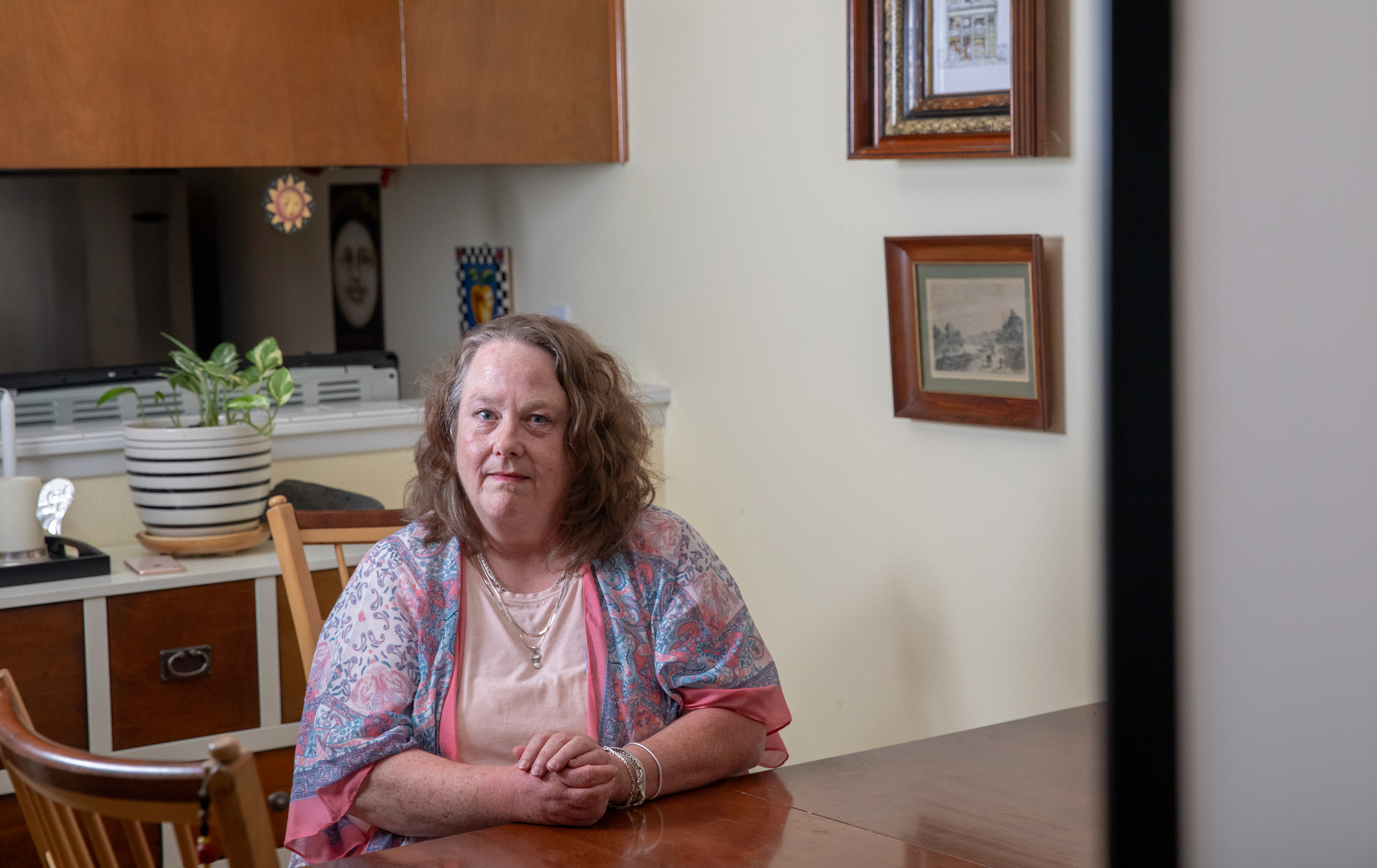 A woman in a pink tshirt and a paisley cardigan sits at a dining room table