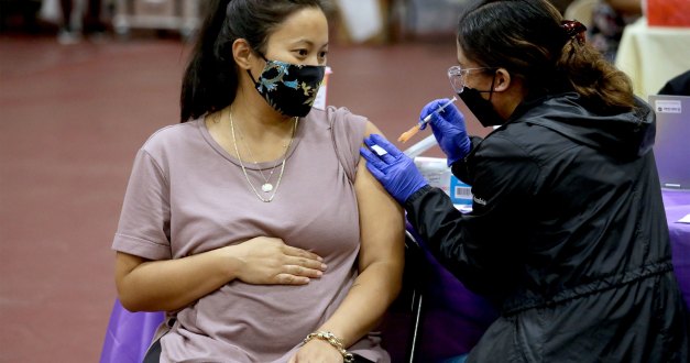 A pregnant woman wearing a face mask received a shot in the arm from a nurse.