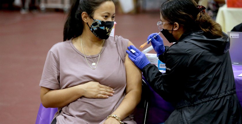 A pregnant woman wearing a face mask received a shot in the arm from a nurse.