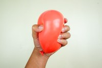 A hand tightly squeezes a small red balloon.