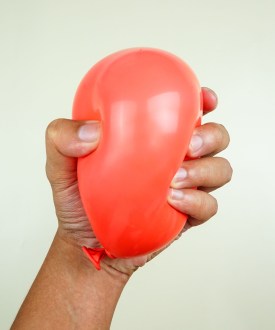 A hand tightly squeezes a small red balloon.