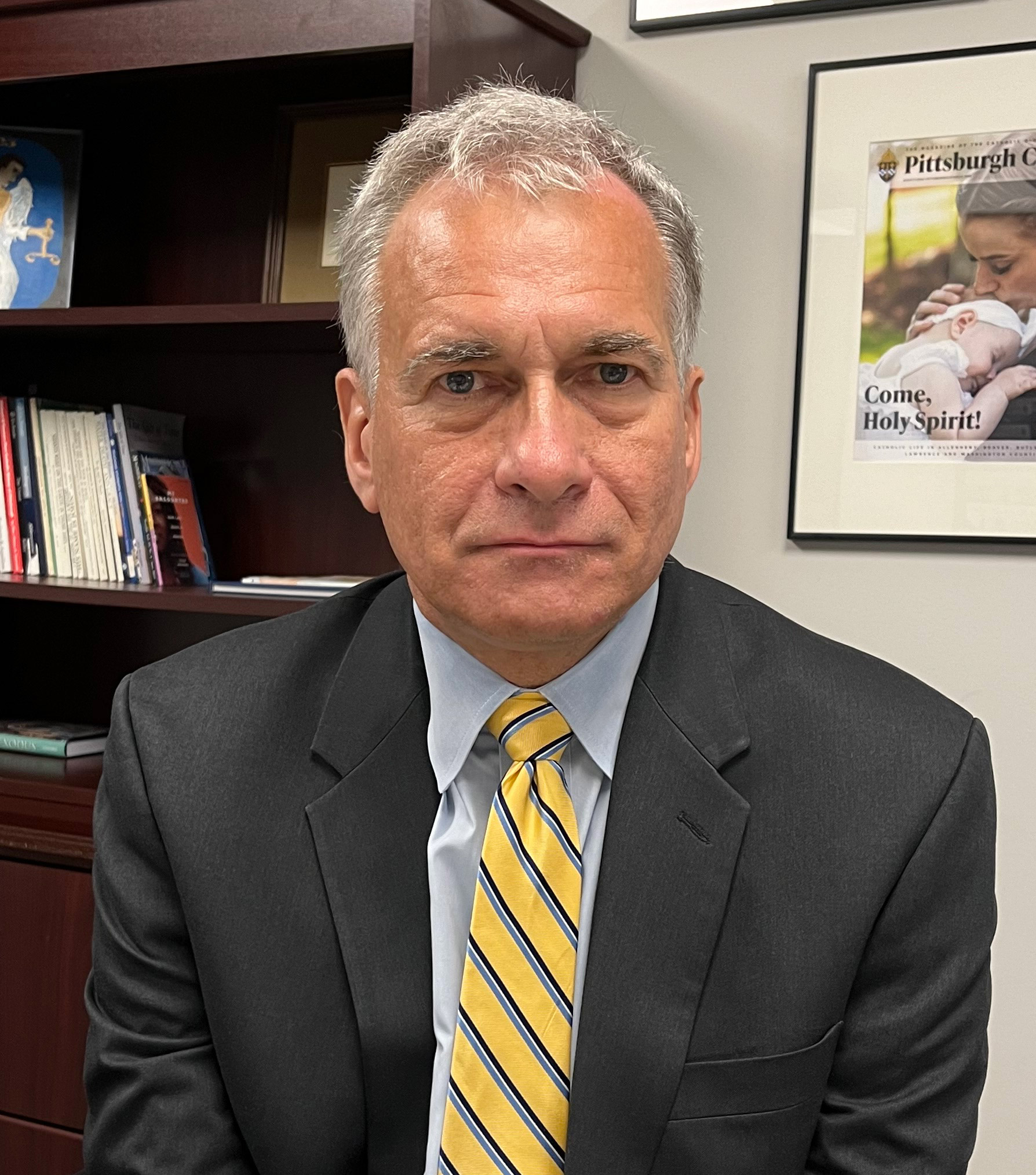 A photo of a man sitting for a photo in his office.