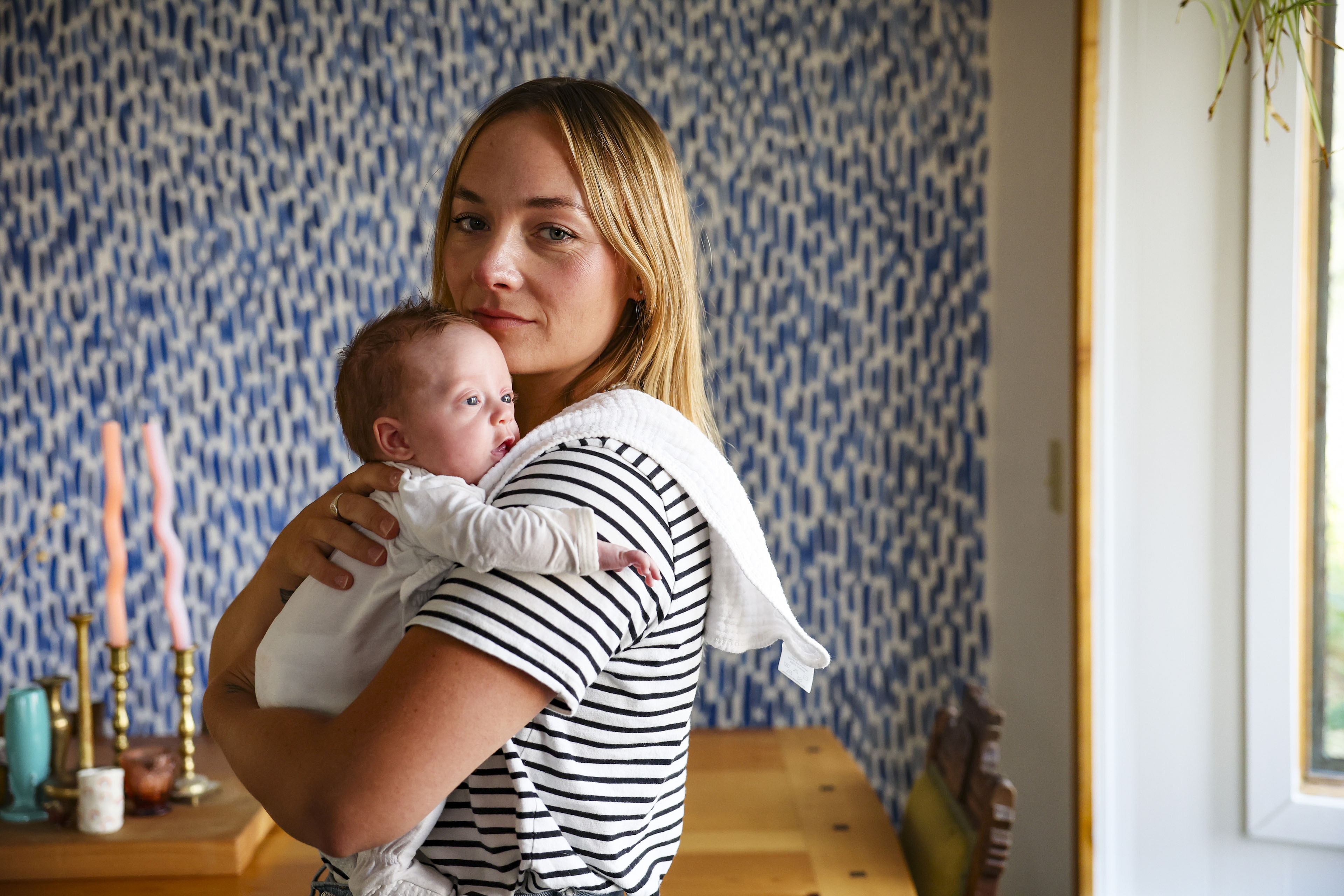 A woman with blond hair wearing a black and white striped shirt holds a baby in her arms