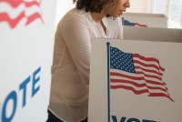 A photo of a woman of color filling out a ballot at a voting booth.