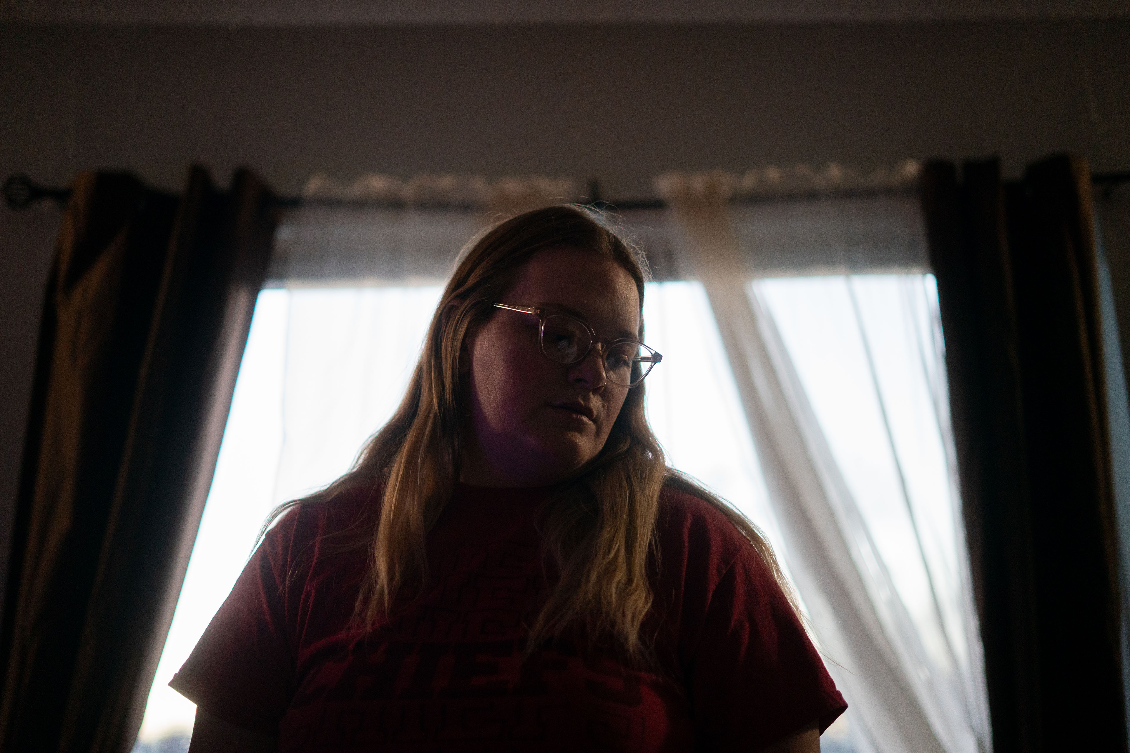 A woman with blond hair and glasses stands in front of a window looking down