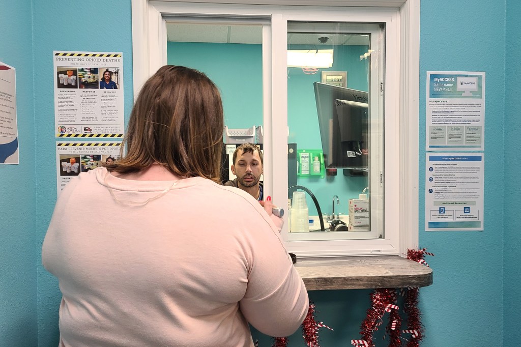 A photo of a woman at a service window, receiving a methadone prescription.