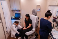 A photo of two medical professionals helping a women sitting in a chair inside a mobile clinic.