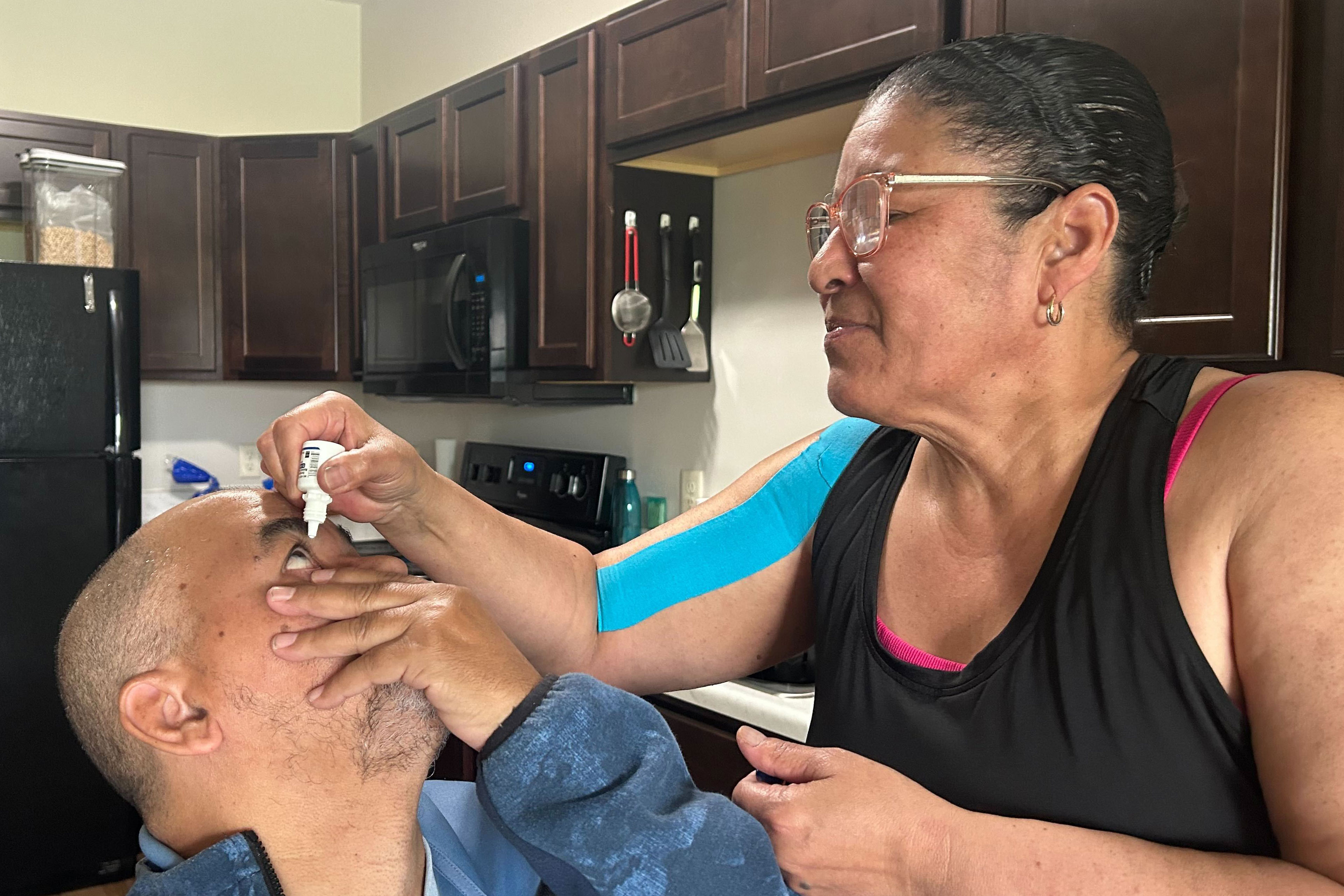 A photo of Wanda Serrano putting eyedrops in her husband's eyes.