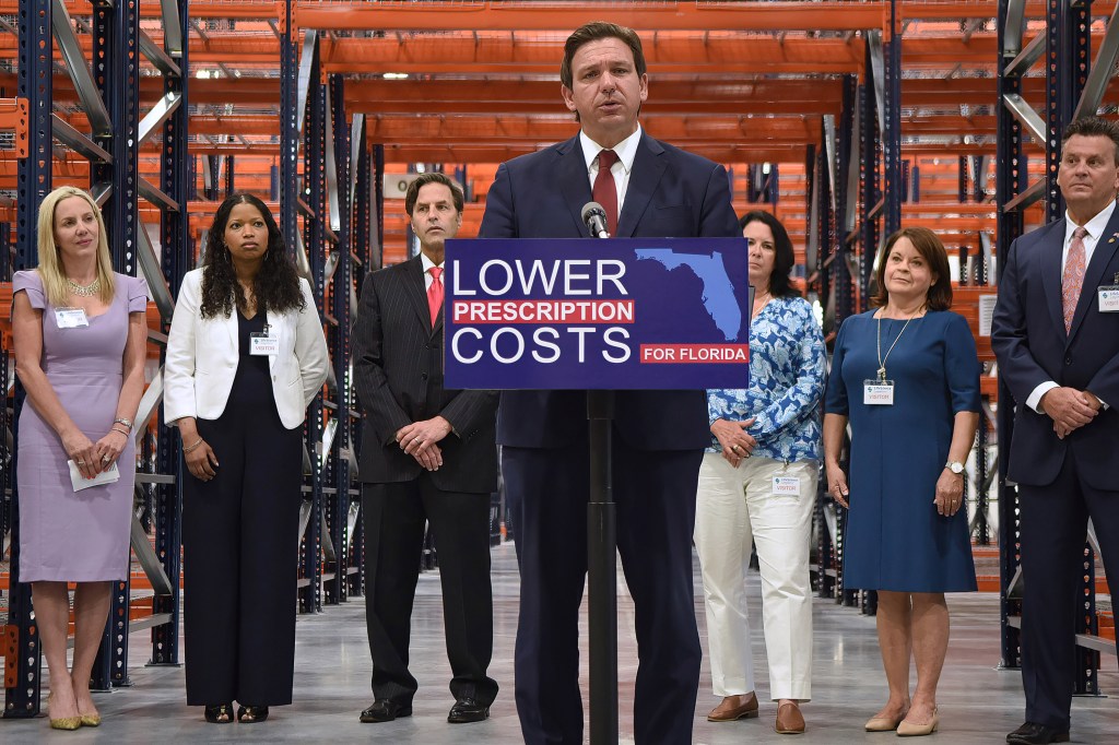 A photo of Ron DeSantis speaking inside a warehouse at a podium with a sign that reads, "Lower drug costs."