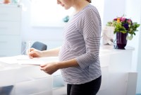 A pregnant woman is at reception for doctor's office, signing a piece of paper.