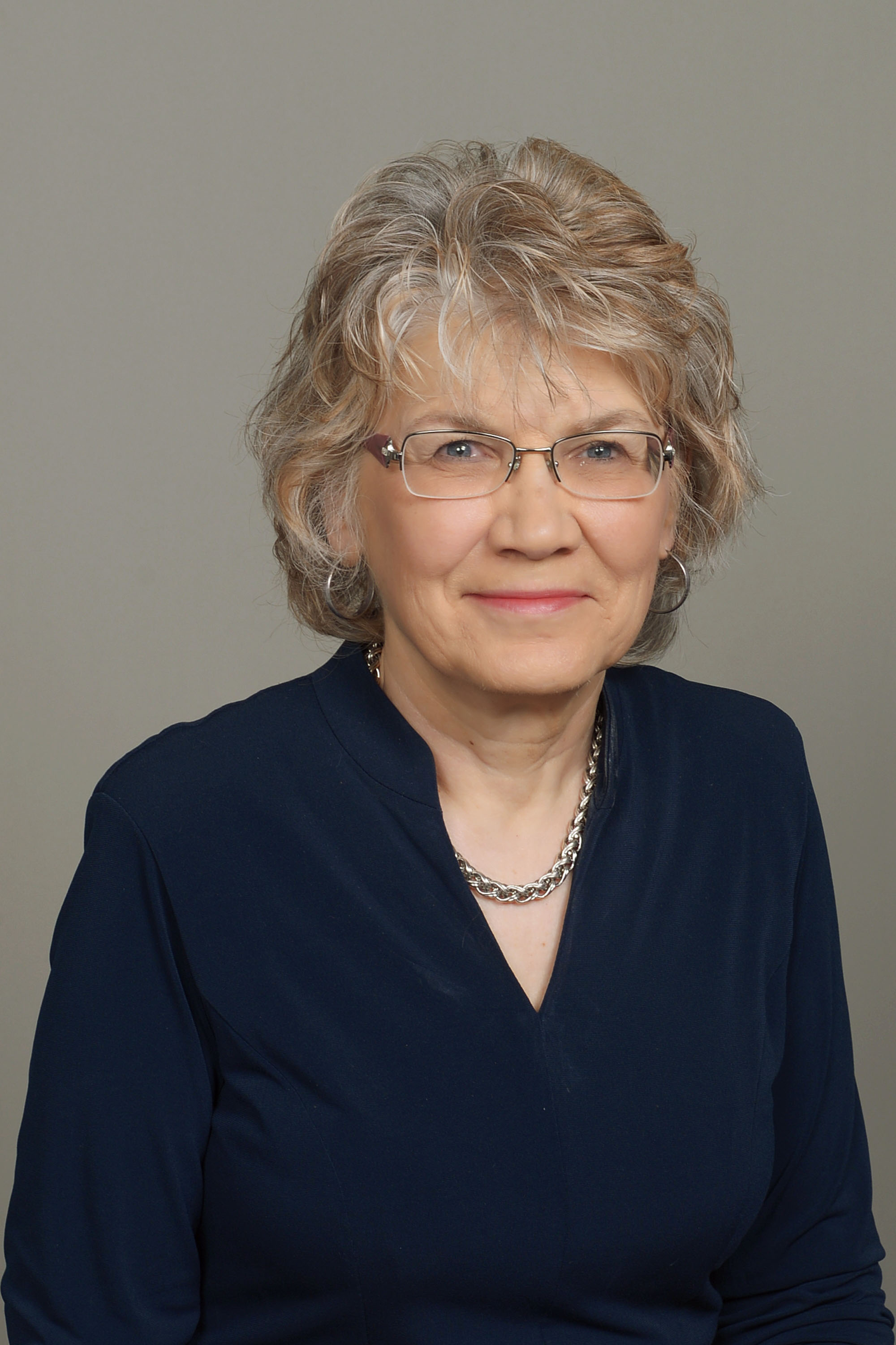 A studio portrait of Linda Camp, a senior woman with short blonde-gray hair and glasses.