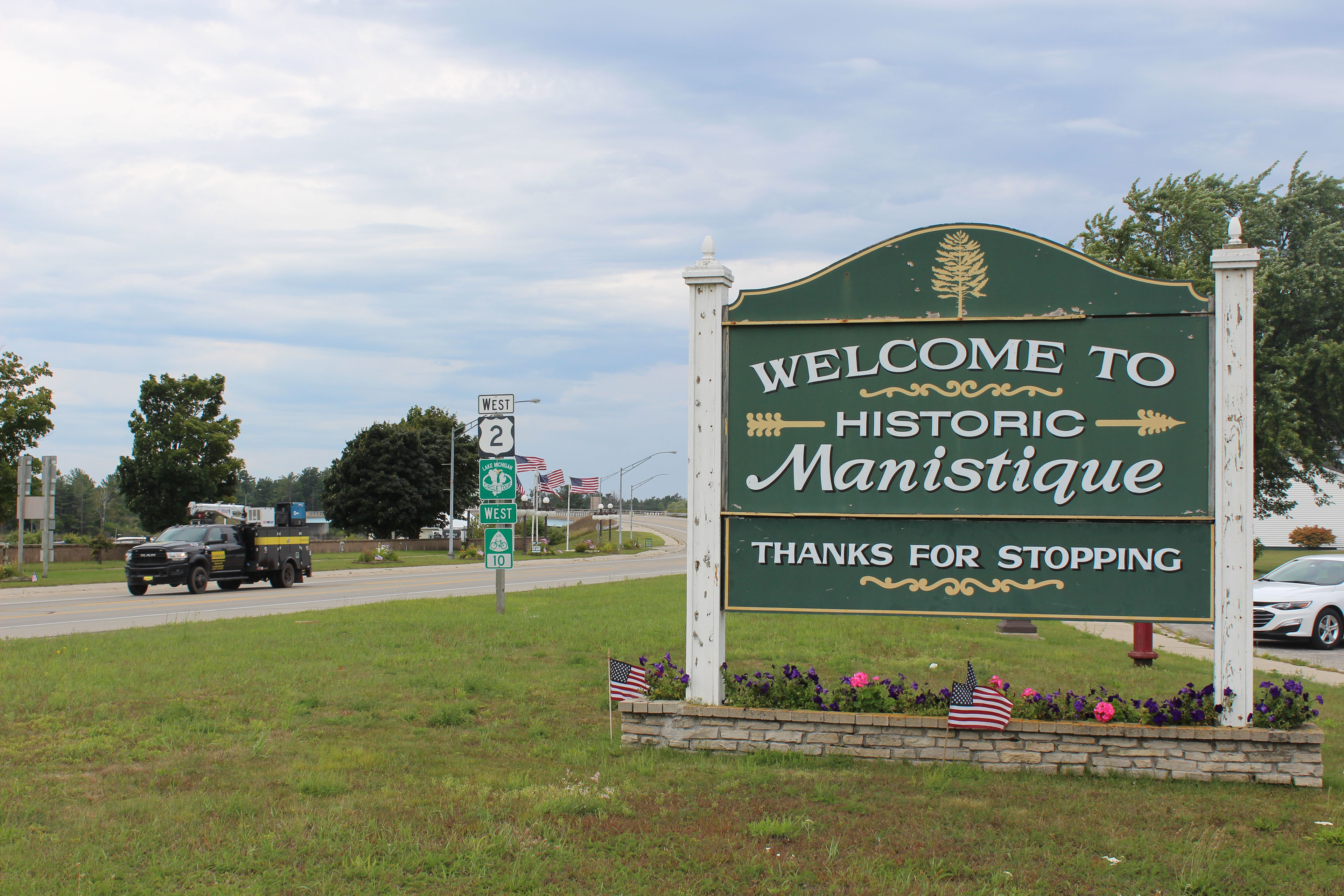 A green sign with yellow writing says "Welcome to historic Manistique"