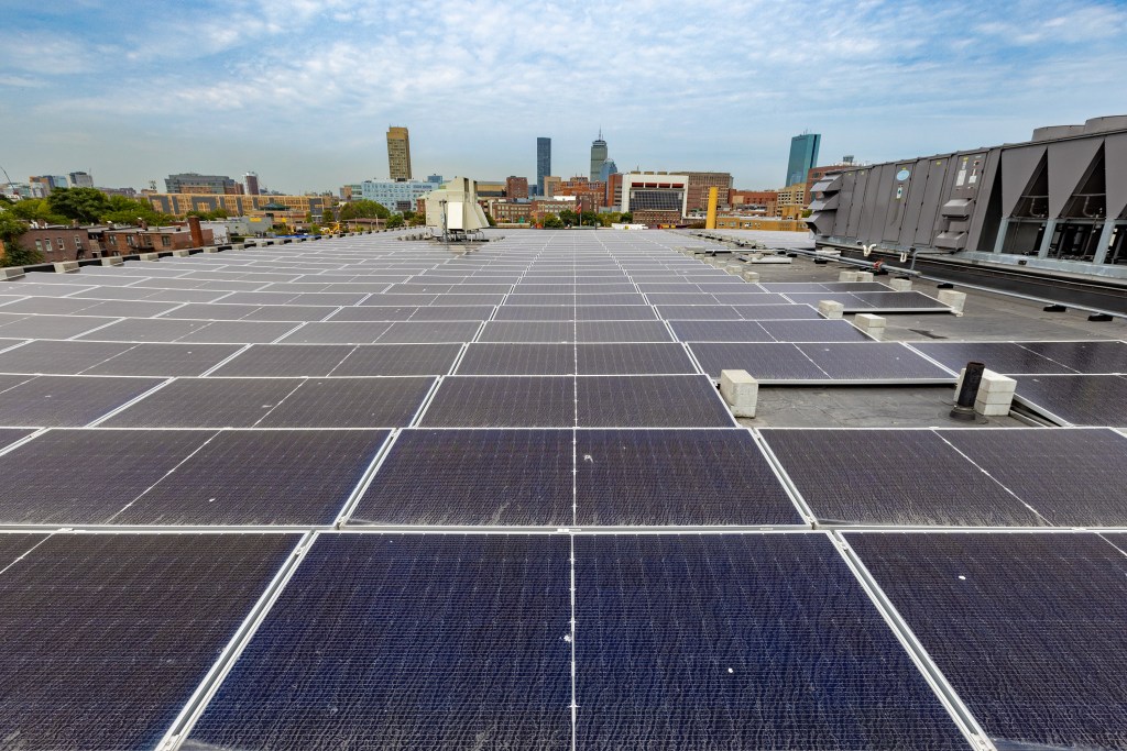 An array of solar panels on the roof of a building with a skyline in the background.