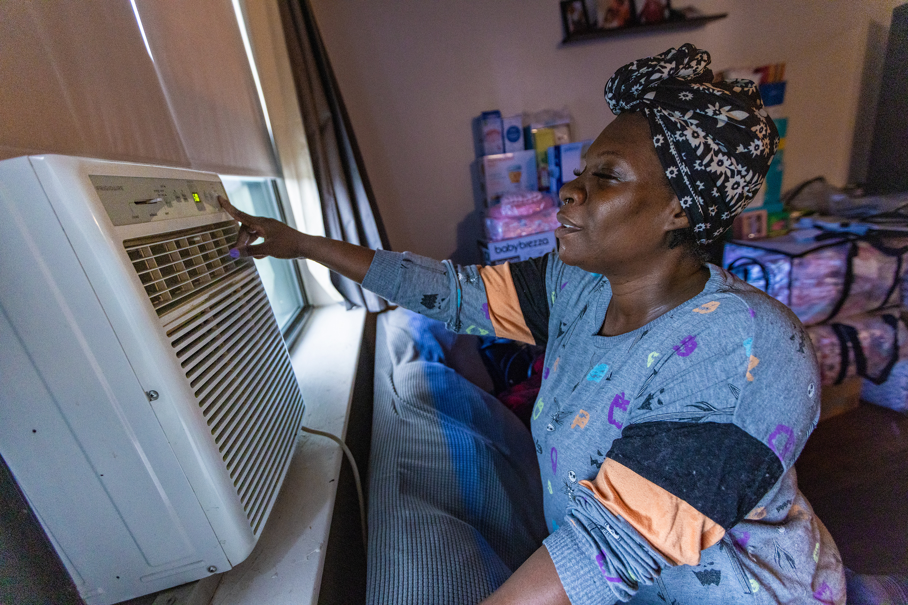 A woman adjusts the settings on an air conditioning unit in a window.