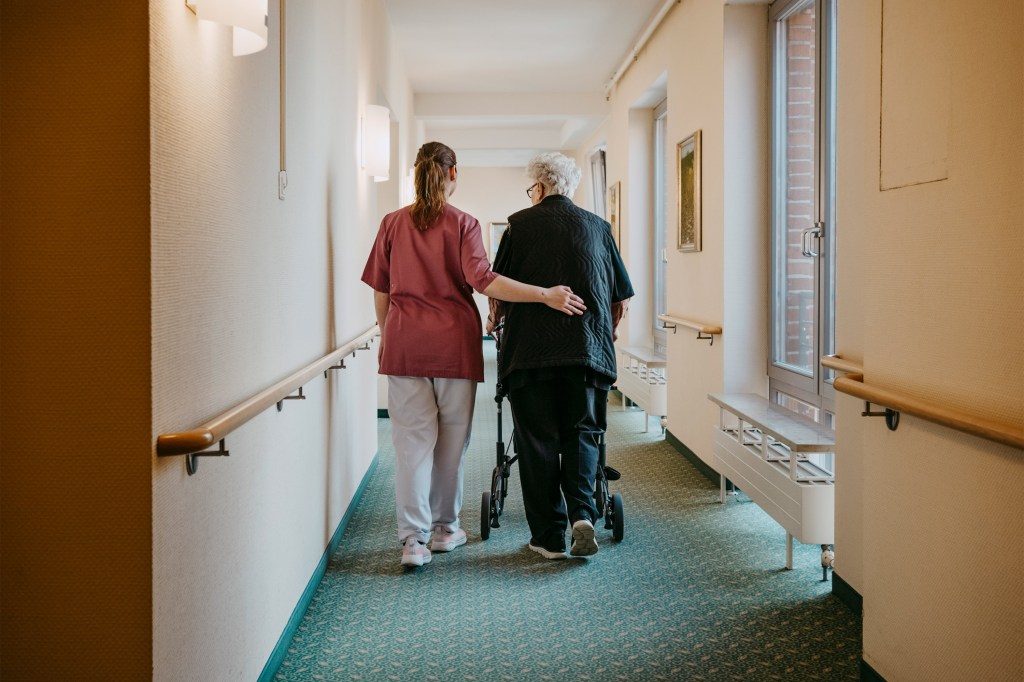 A photo of nurse walking a patient down the hallway of a nursing home.