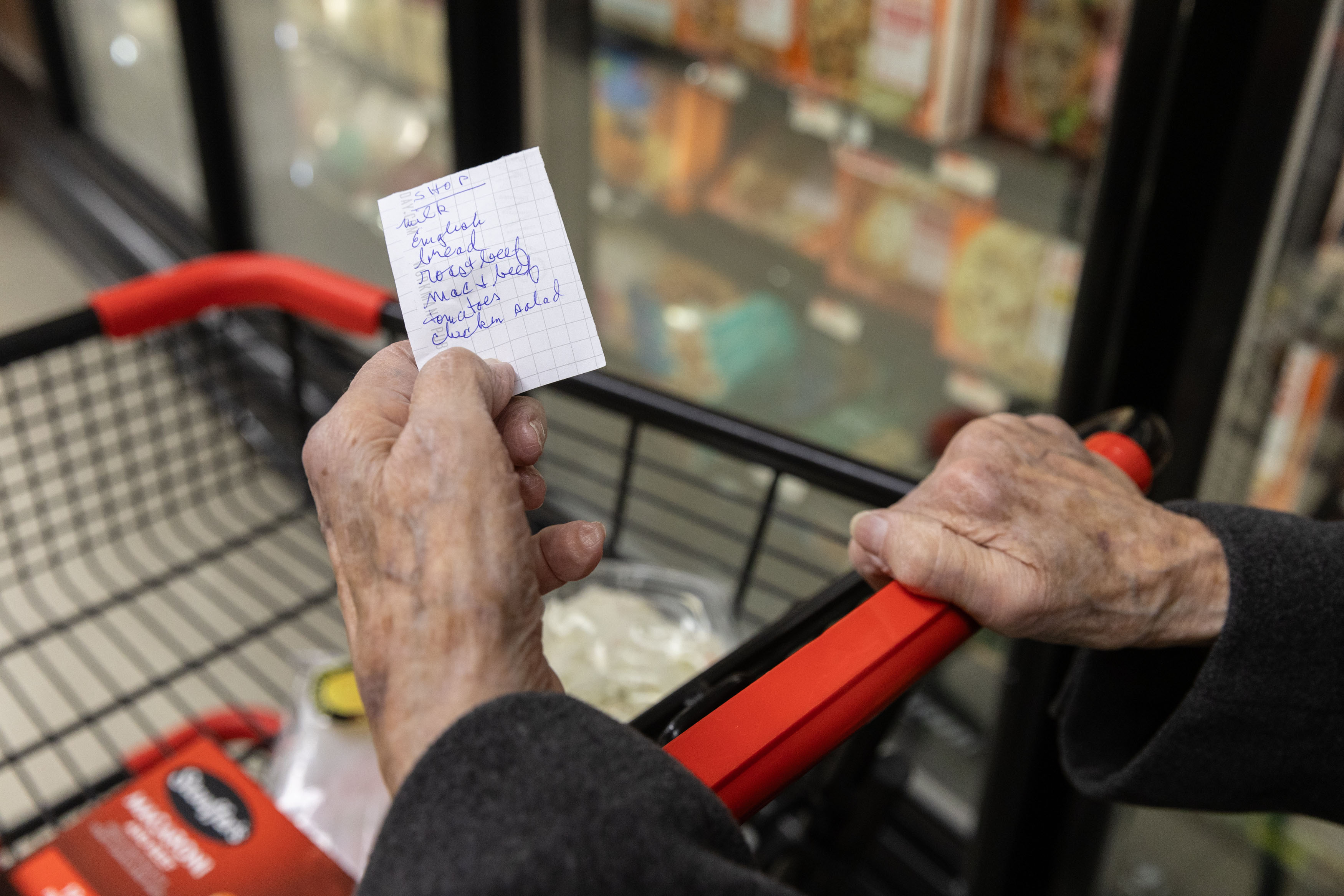 An over-the-shoulder photograph of a senior woman's hands holding a grocery list.