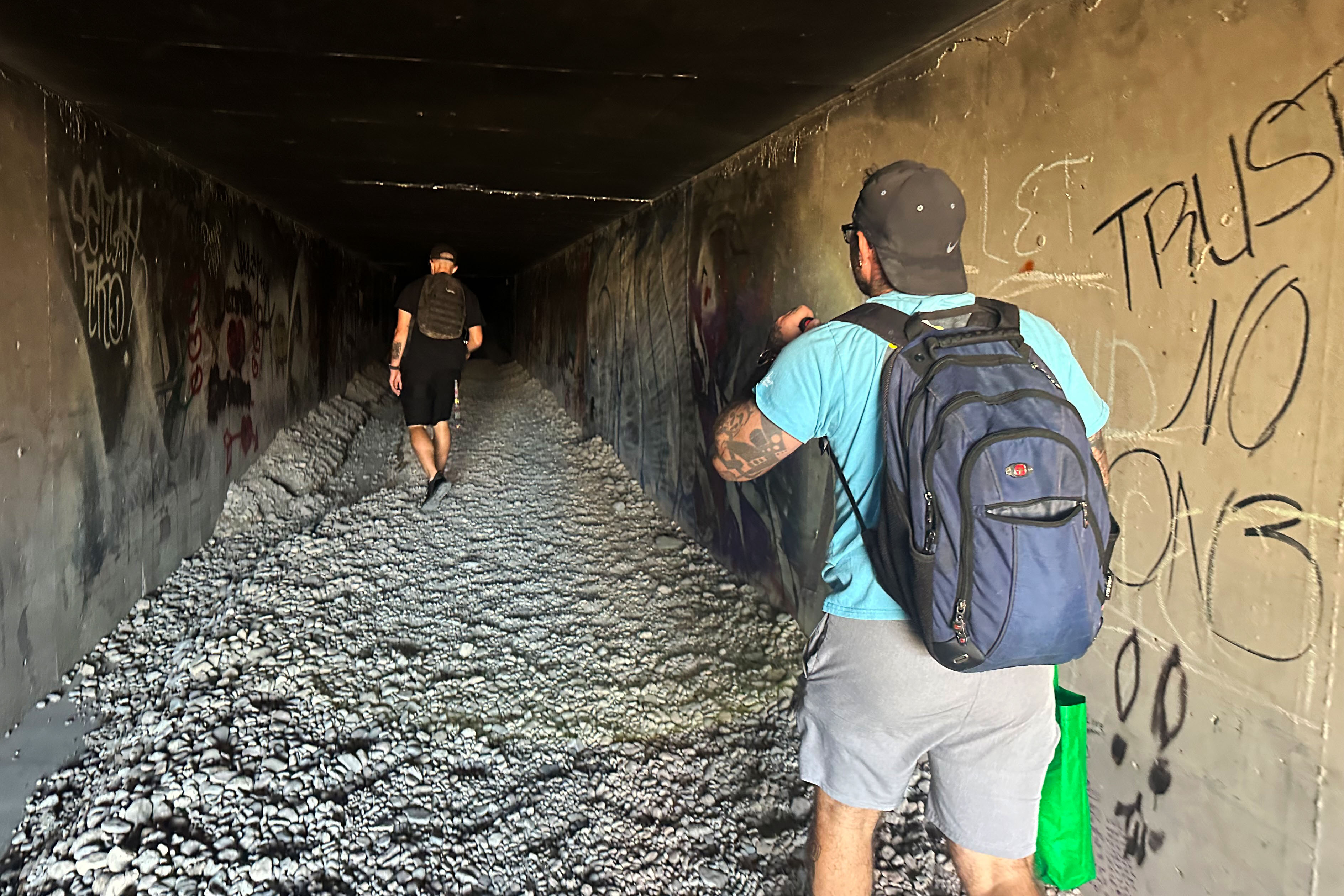 Two men walk in an underground tunnel with their backs to the photographer as they head into darkness.