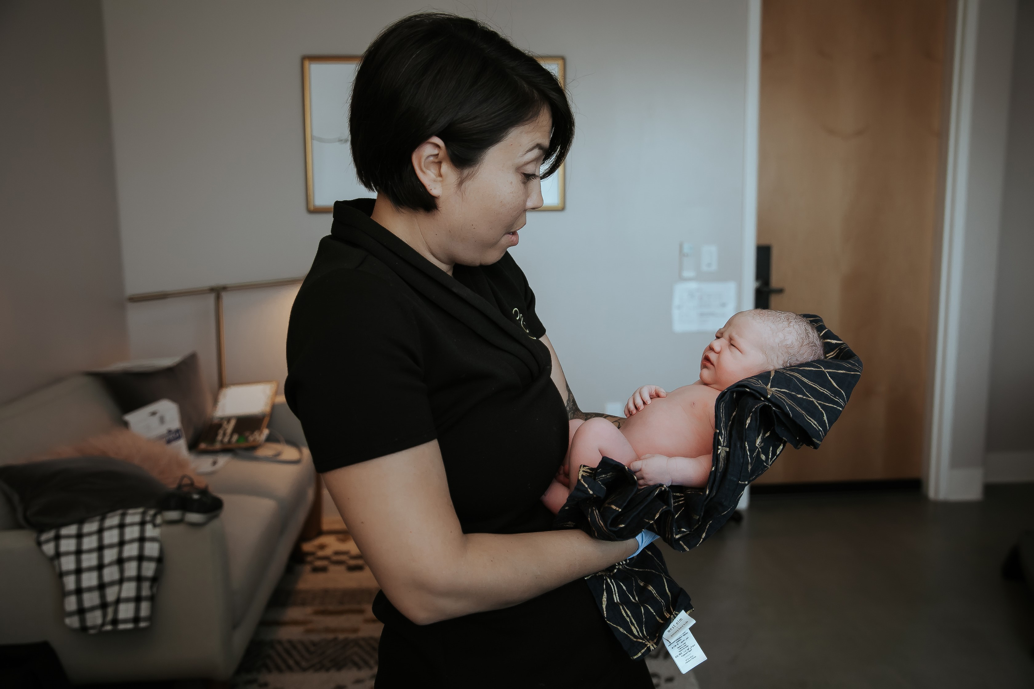 A woman in dark scrubs with short brown hair cradles a newborn baby in her arms.