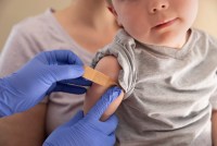 A close up photo of an unidentifiable toddler sitting in his mother's lap while a doctor puts a band-aid on his arm after receiving a vaccination.