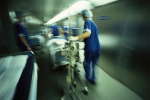 A photo of medical staff in a hospital rushing a patient in a bed down a hallway.