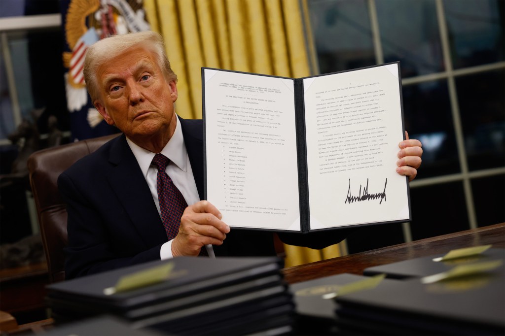 A photo of President Donald Trump holding up a signed executive order to the camera.